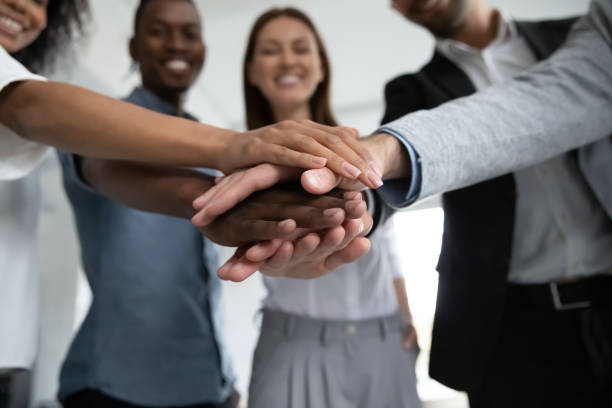 Close up happy diverse business people putting hands together, showing support and unity. Multiracial colleagues involved in team building activity. Staff training concept, start working together.